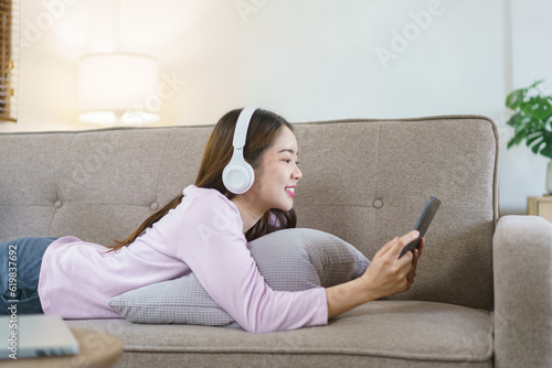 Women lying on big sofa and wearing headphone to watching movie on tablet in lifestyle at home