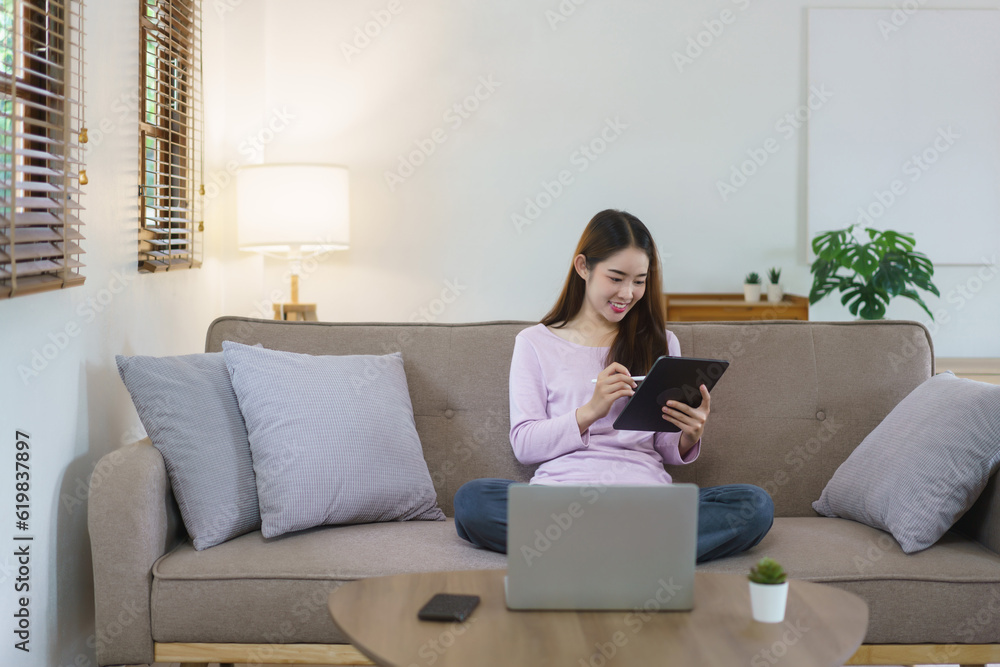 Women sitting on big sofa and writing notes on tablet with electronic pen in lifestyle at home Women sitting on big sofa and writing notes on tablet with electronic pen in lifestyle at home