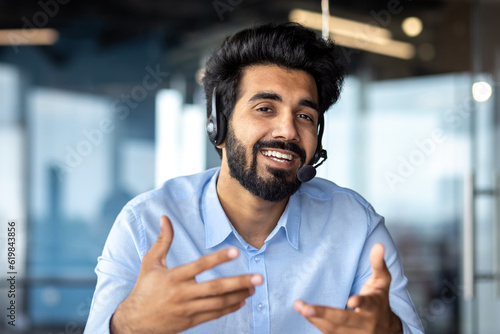 Webcam view, video call online meeting businessman smiling and talking friendly with colleagues clients, successful hispanic worker looking at camera working inside office with headset phone.