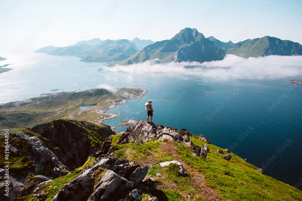Silhouette of a hiker woman stand on top of mountain hike summit overlooking epic Lofoten Archipelago landscape. Inspiring and amazing idea of adventure. Roadtrip in Norway