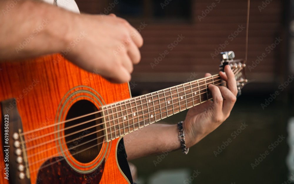 A man plays the guitar sitting on a wooden pier near the lake, the concept of summer outdoor recreation.