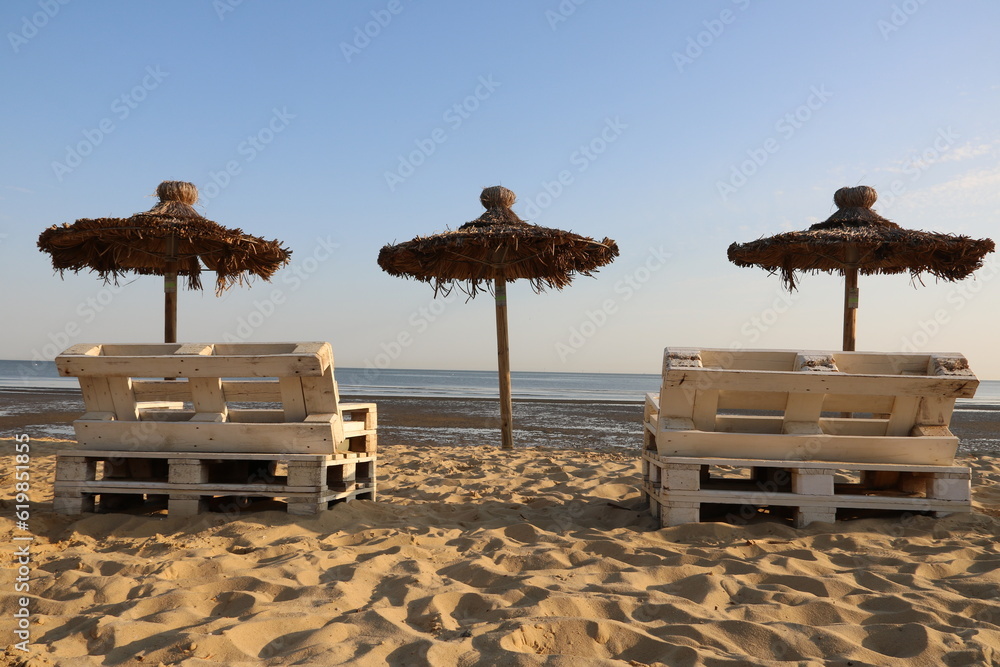 Sonnenschirme aus Stroh und Liegen am Strand der Nordsee in Cuxhaven