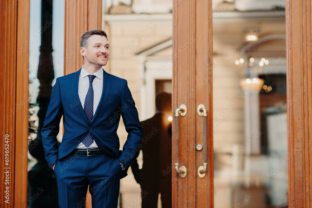 Satisfied worker in luxury suit waits by restaurant entrance, celebrates with colleagues, looks happily aside. Satisfied worker in luxury suit waits by restaurant entrance, celebrates with colleagues, looks happily aside.