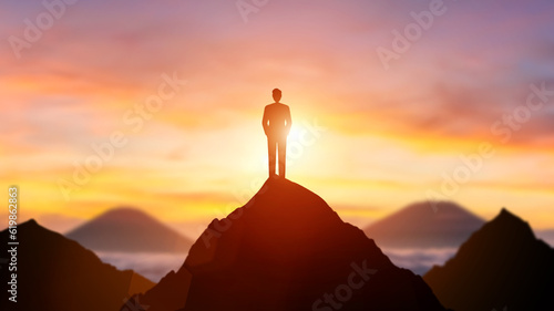 Silhouette man standing on top of mountain in sunset or dawn sky with sunshine and dark orange shade mountain peak background. Business goals achievement concept. People lifestyle work life balance.