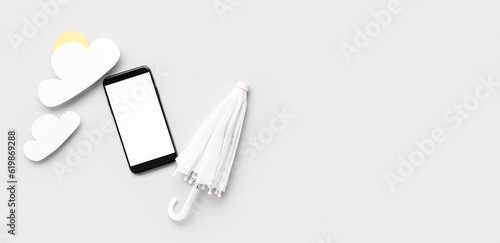 Mobile phone with blank screen  small umbrella and paper clouds on light background. Weather forecast concept