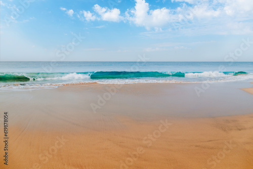 Ocean waves on the sandy beach coast under the beautiful blue sky with clouds of Sri Lanka island.