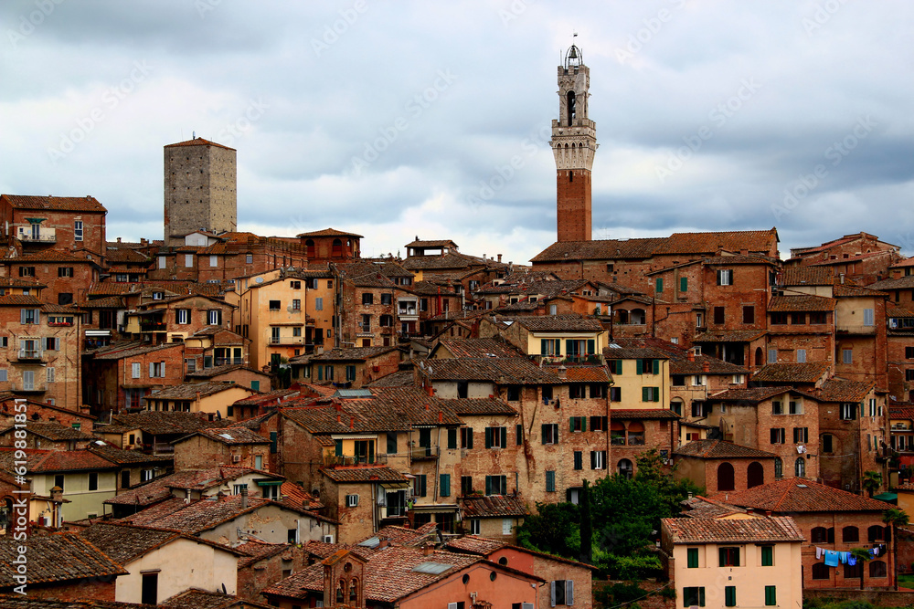 Photo of the historic part of the city with the tower of Torre del Mangia in the center of the photo against a stormy sky in the city of Siena, Tuscany region, Italy