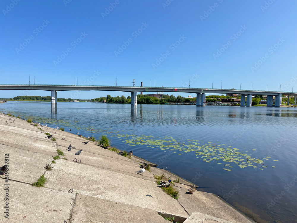 on a summer day, the reflection of the automobile bridge in the blue water of the river
