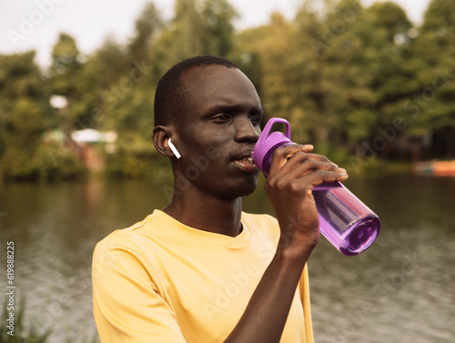 Young handsome African American sport man tired and thirsty after running workout holding bottle drinking water