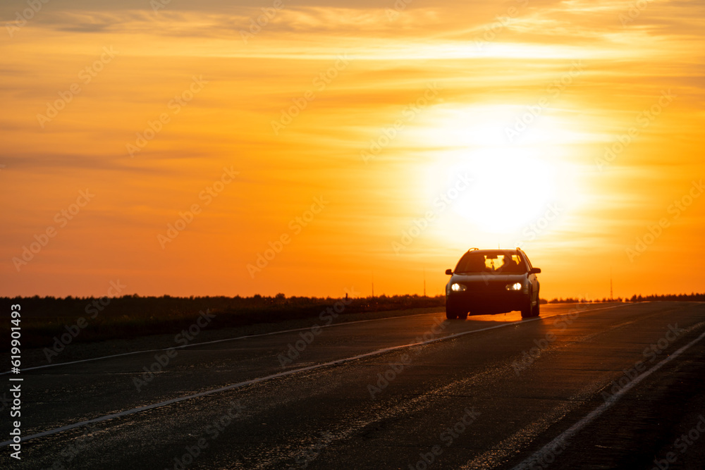 Fototapeta premium The silhouette of a car on the road against the background of the sun. The car is driving on the highway during sunset. The concept of travel and freedom.