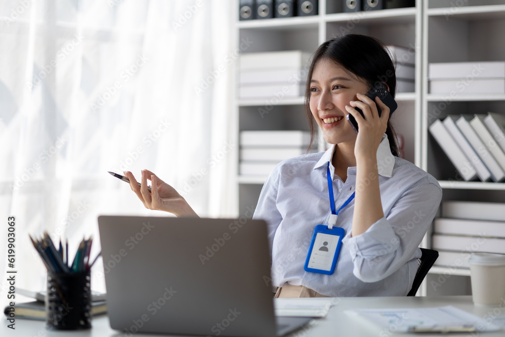 Asian woman talking on the phone, she is a salesperson in a startup company, she is calling customers to sell products and promotions. Concept of selling products through telephone channels. Asian woman talking on the phone, she is a salesperson in a startup company, she is calling customers to sell products and promotions. Concept of selling products through telephone channels.