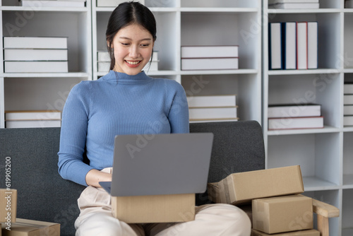 Asian woman online store business owner, online shop owner working from home, posting products for sale on website and accepting orders and packing products for customers with private courier service.