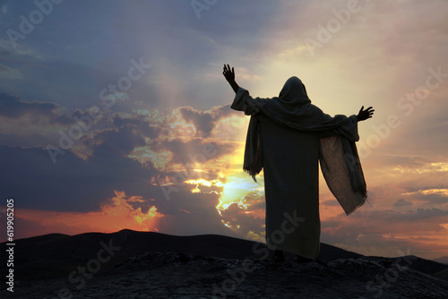 Jesus praying alone with raised hands on a hill at sunset. Biblical concept. photo