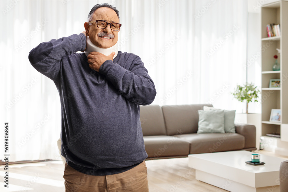Mature man wearing a cervical collar and standing in a living room Mature man wearing a cervical collar and standing in a living room