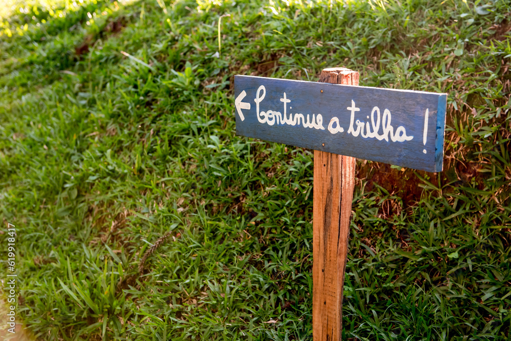 Wooden plaque driven into the grass, Translation: Continue the trail