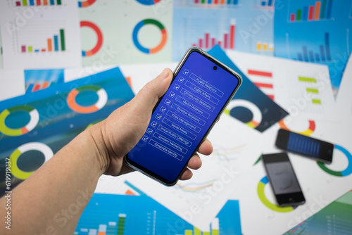 Ręka trzymająca telefon z niebieskim ekranem z napisami na tle wykresów.