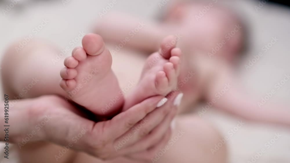 Hand of mother holding tender bare feet of infant baby lying on soft bed at home caring woman expressing love to little boy sleeping in nursery in morning closeup Hand of mother holding tender bare feet of infant baby lying on soft bed at home caring woman expressing love to little boy sleeping in nursery in morning closeup
