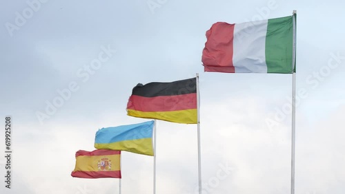 Flags of Italy, Germany, Ukraine, Spain waving in wind on blue sky background, closeup