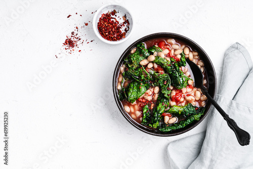 Vegan dinner, beans with tomatoes and kale in ceramic bowl, top view photo