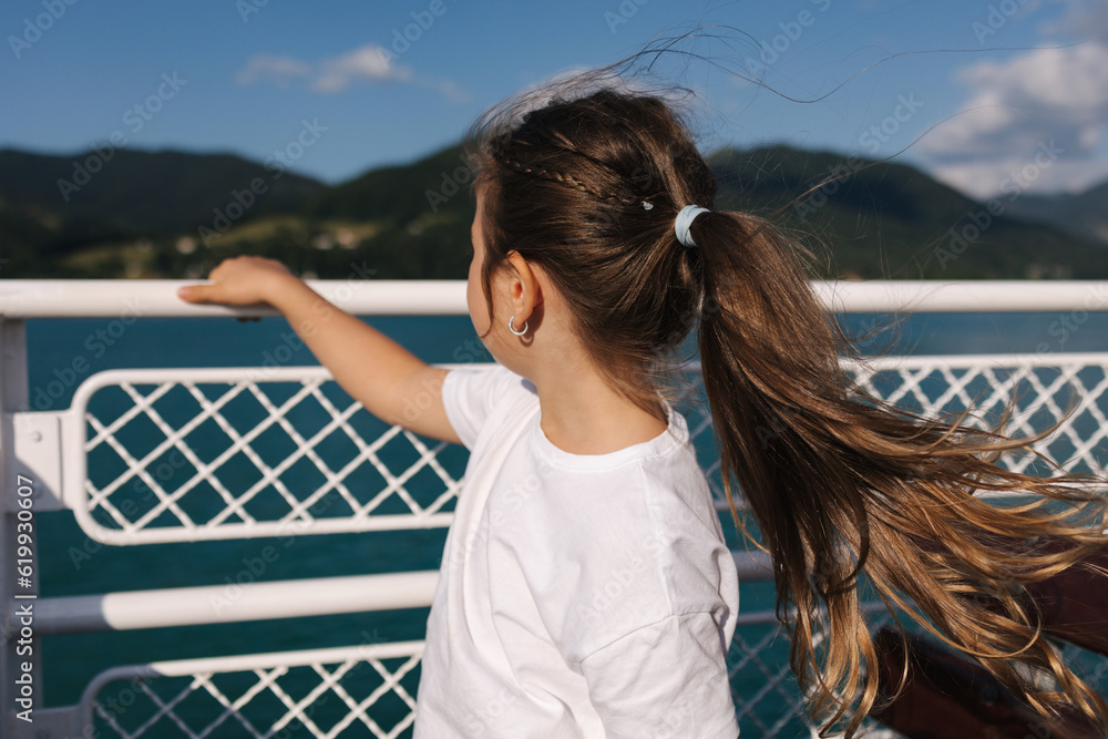 Little girl looking on the water during the excursion along the lake on ship. The wind blows the hair