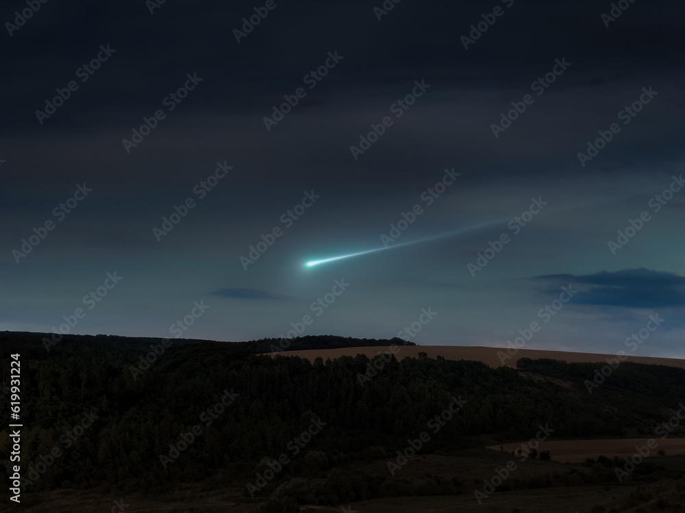 Fireball in the evening sky over the hills. Meteor trail above the horizon, beautiful landscape.