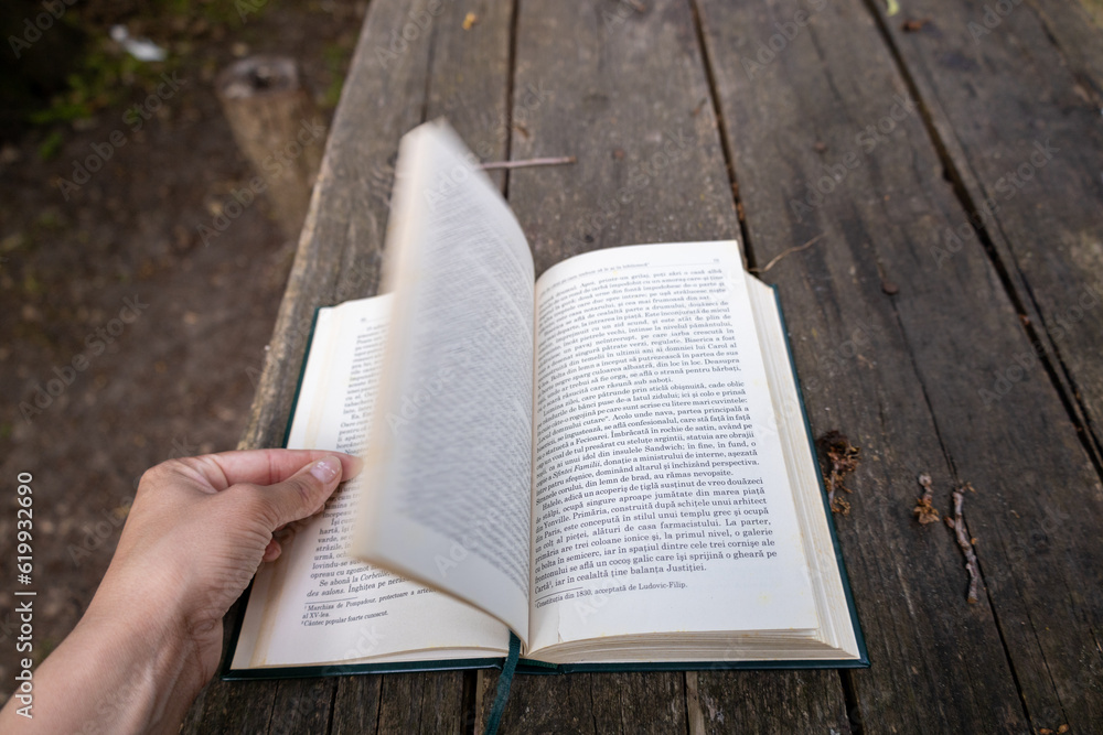Fototapeta premium Close up photo of a caucasian woman reading a book on a table in the forest.