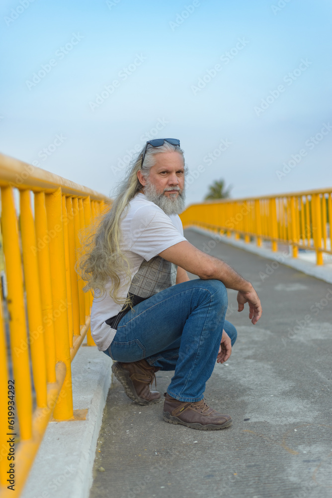 Long-haired gray-haired man on a pedestrian bridge.
