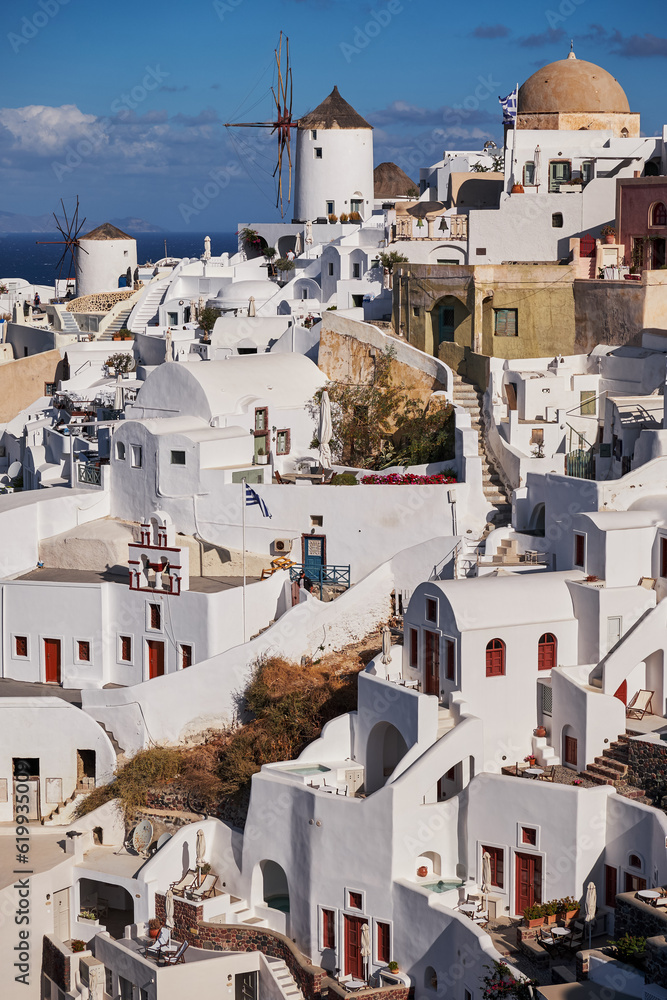 Beautiful panorama view from the old castle of Oia village with traditional white houses and windmills in Santorini island in Aegean sea at sunset, Greece