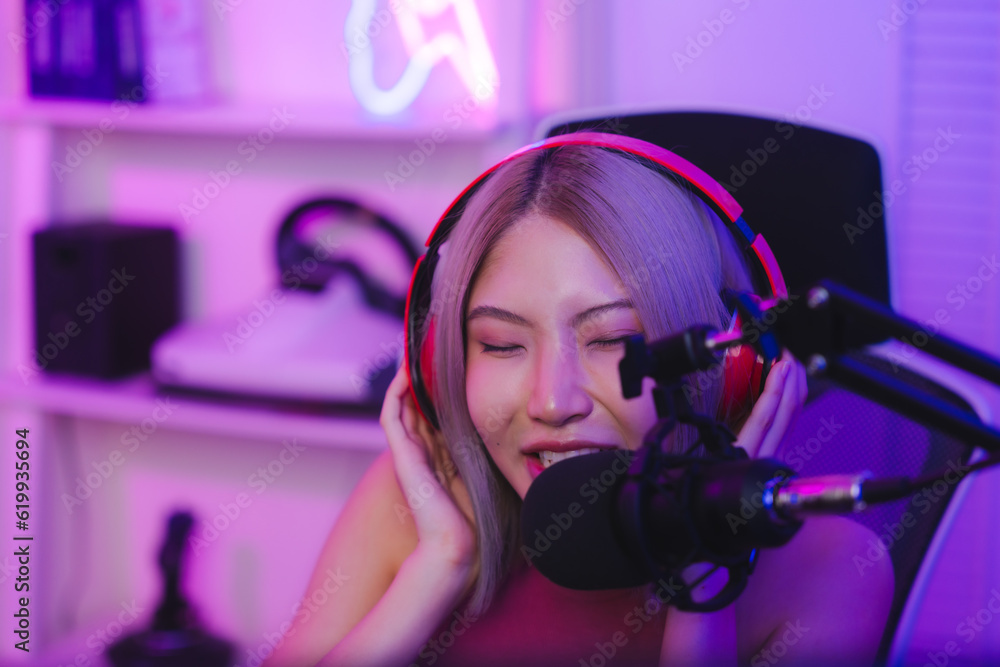 Young cute woman talking to players and audience on computer in neon led light room at home, Excited smiling gamer Asian girl waring headset with a mic playing an online video game live streaming Young cute woman talking to players and audience on computer in neon led light room at home, Excited smiling gamer Asian girl waring headset with a mic playing an online video game live streaming