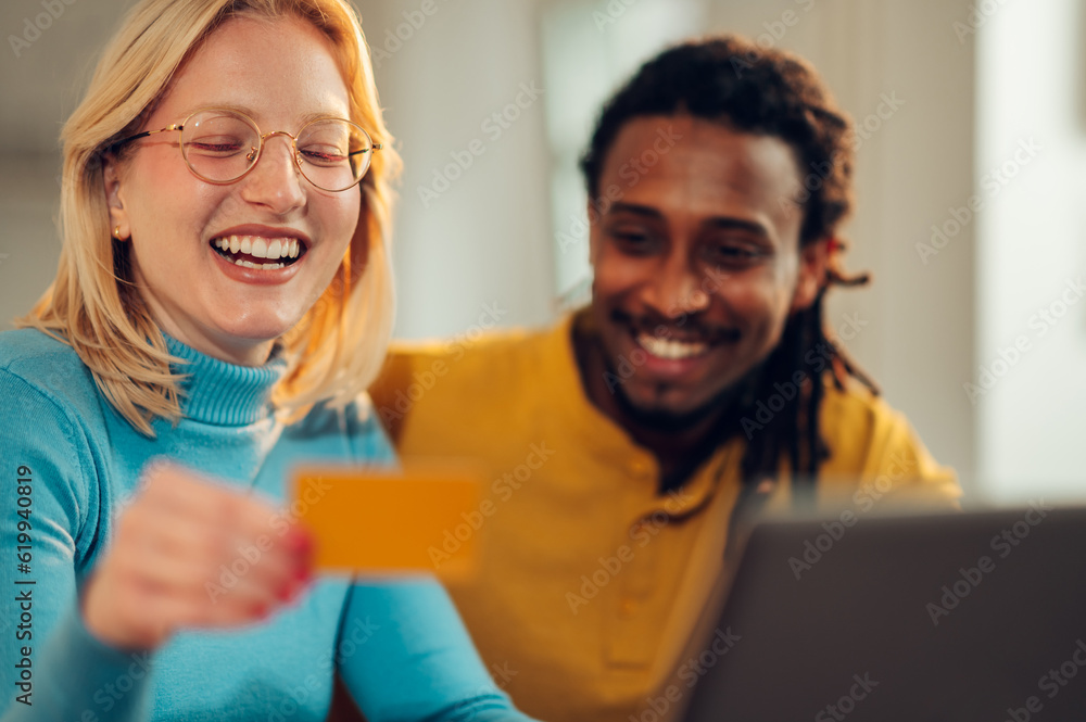 Fototapeta premium A cheerful interracial couple is sitting at home and shopping online with a credit card.