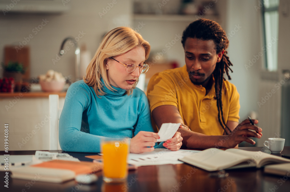 Fototapeta premium A serious multicultural couple is sitting at home and looking at high bills and taxes.