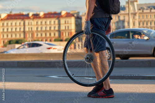 A man carries a bicycle wheel in his hand , close - up . Return a bike part for repair.