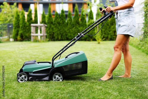 Beautiful laughing housemaid with lawn mower near country house. Make a fun