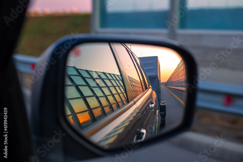 View in the mirror of the side view of the car on the road and caravan at dawn. Trucking and travel