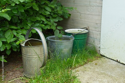 buckets and watering can standing in the garden to collect rainwater, climate warming and ways to deal with the lack of drought and natural watering of the garden © Michal