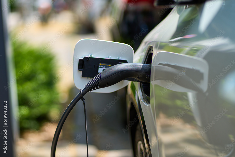 White e-car that is on the charging cable. The electric car is shown from the side where the environmentally conscious vehicle is being charged. White e-car that is on the charging cable. The electric car is shown from the side where the environmentally conscious vehicle is being charged.