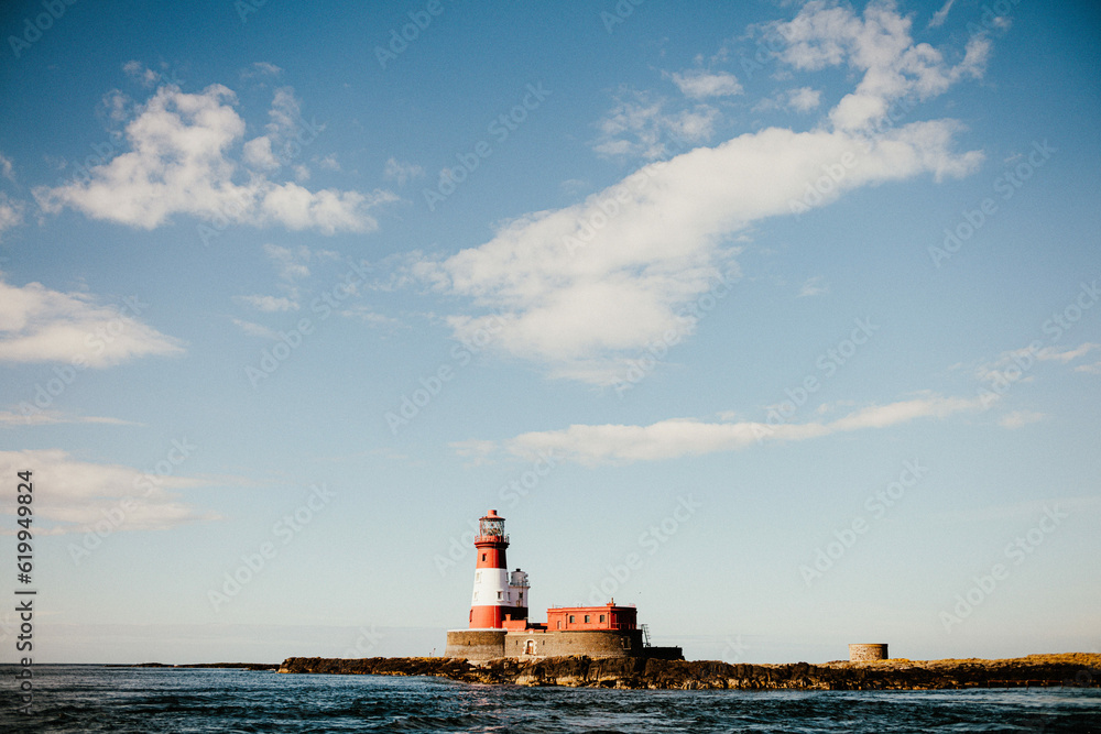 Red and White lighthouse on an island surrounded by sea and blue skies