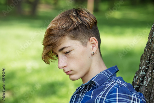 Portrait of serious teenager sitting on grass in park. Gen Z. Unhappy and stress. © Olha Tsiplyar