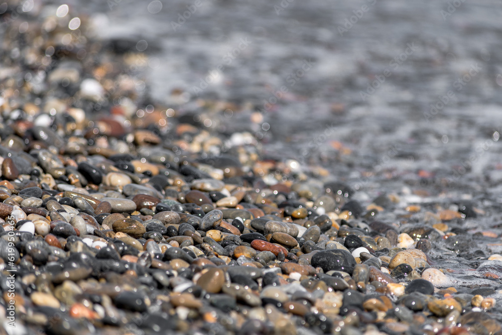 Close-up of pebble beach with light reflecting on colored stones against the waves in the background Close-up of pebble beach with light reflecting on colored stones against the waves in the background