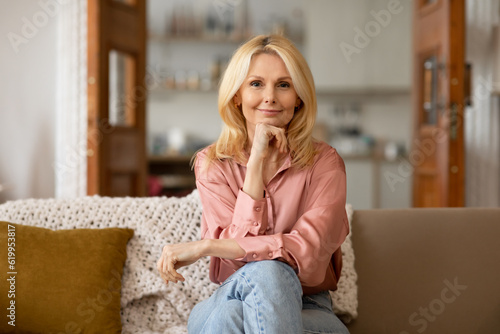 Happy Mature Blonde Woman Posing Sitting On Sofa At Home