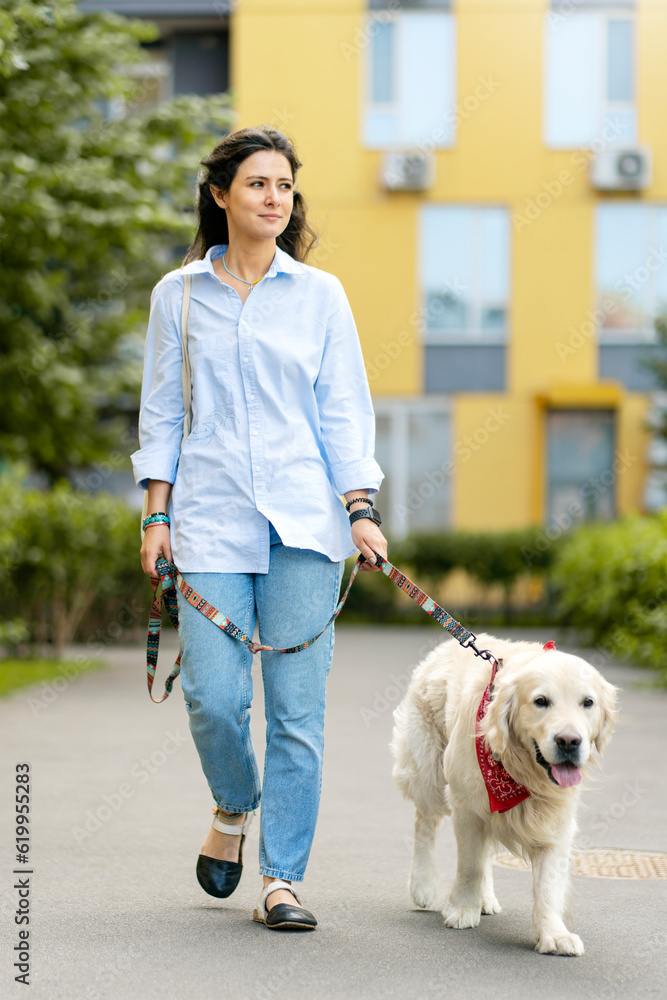 Cute pretty woman wearing casual clothes leading well groomed dog, golden retriever on street Cute pretty woman wearing casual clothes leading well groomed dog, golden retriever on street