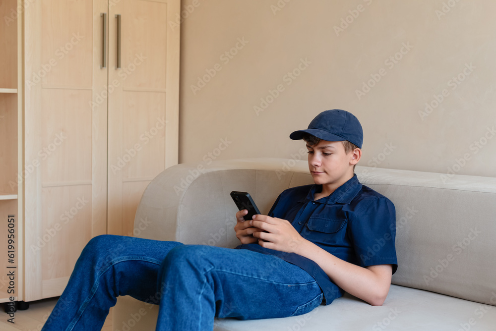 Teenager boy using smart phone on sofa living room at home. Boy holding and using cellphone for searching data and social media on internet. Teenager and Technology concept. Communication with friends Teenager boy using smart phone on sofa living room at home. Boy holding and using cellphone for searching data and social media on internet. Teenager and Technology concept. Communication with friends