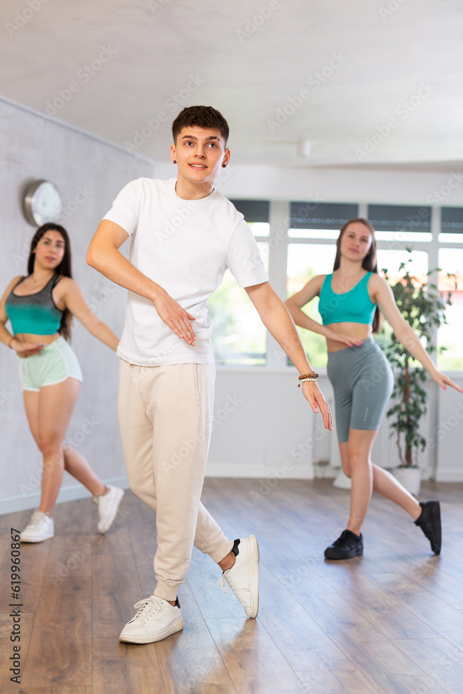 Guy and young girls in good mood actively move and dance reggaeton at choreography lesson. Leisure activity, hobby