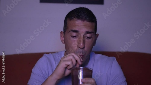 Young guy enjoying a fresh cocoa. Video of a middle-aged man refreshing himself with a glass of cocoa with milk and straw while enjoying his favorite TV series.
