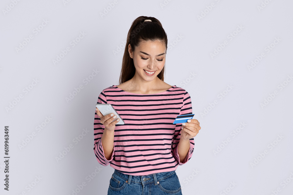 Cheerful pretty brunette woman using smartphone and bank card Cheerful pretty brunette woman using smartphone and bank card