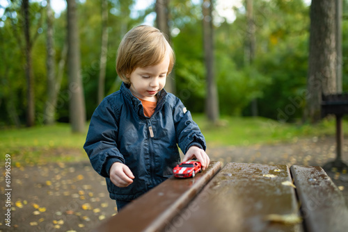 Fototapeta Naklejka Na Ścianę i Meble -  Cute toddler boy playing with red toy car outdoors. Kid exploring nature. Small child having fun with toys. Autumn activities for children.