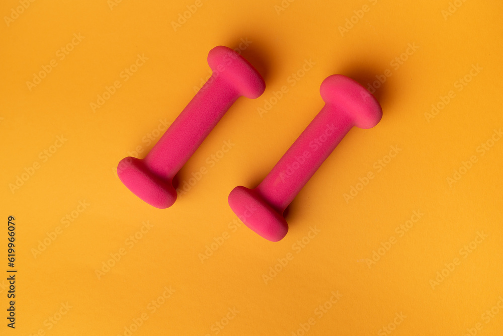 two pink dumbbells for fitness on yellow background two pink dumbbells for fitness on yellow background