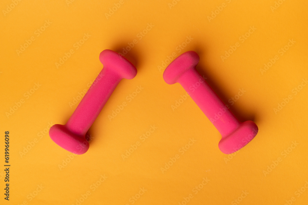 two pink dumbbells for fitness on yellow background two pink dumbbells for fitness on yellow background