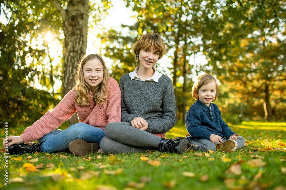 Two big sisters and their toddler brother having fun outdoors. Two young girls with a toddler boy on autumn day. Children with large age gap. Big age difference between siblings. Two big sisters and their toddler brother having fun outdoors. Two young girls with a toddler boy on autumn day. Children with large age gap. Big age difference between siblings.