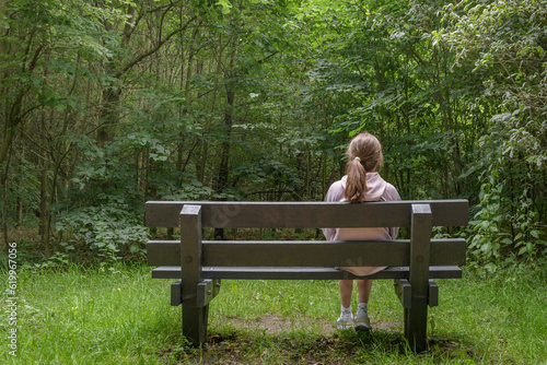 A teenage girl on a bench in a forest park looks deep into the forest. Enjoying the nature